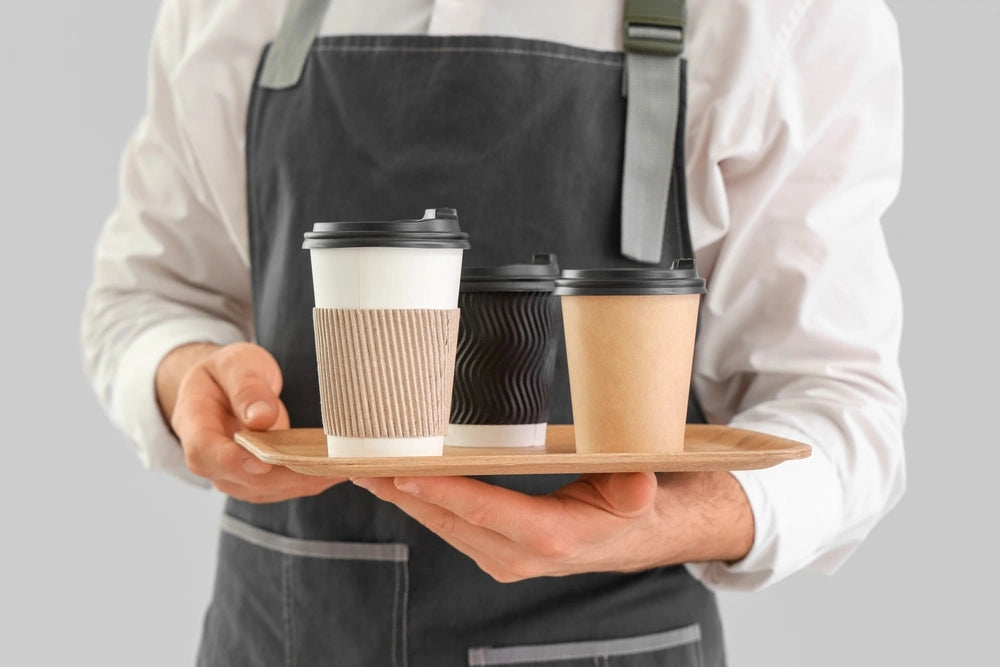 Young male barista with coffee cups.