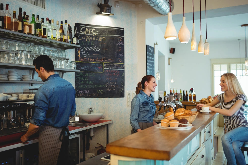 Happy female barista communicating with a young customer at the cafeteria